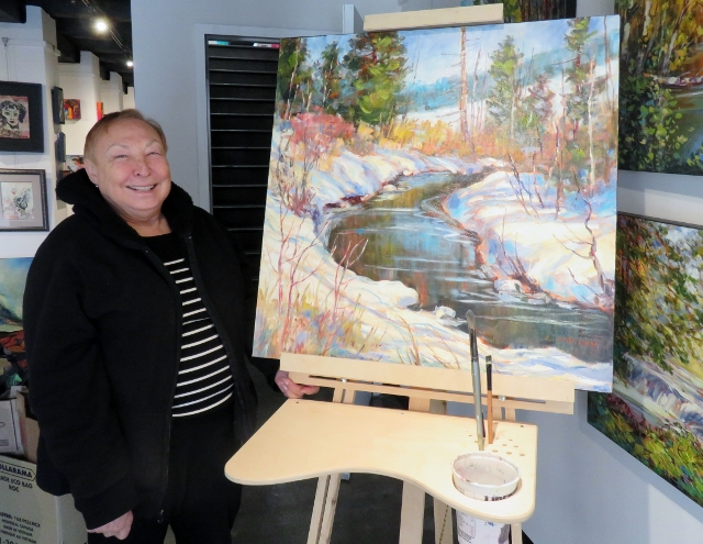 Valerie Kent standing beside a landscape painting in an art gallery